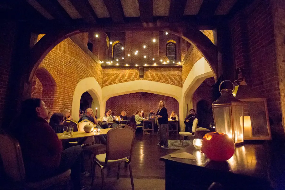 woman standing among tables with arms wide in softly lit room