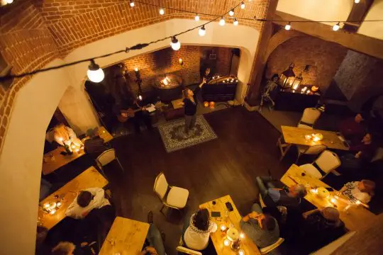 birds eye view of castle hall with people sitting on tables and chairs and a storyteller in the centre